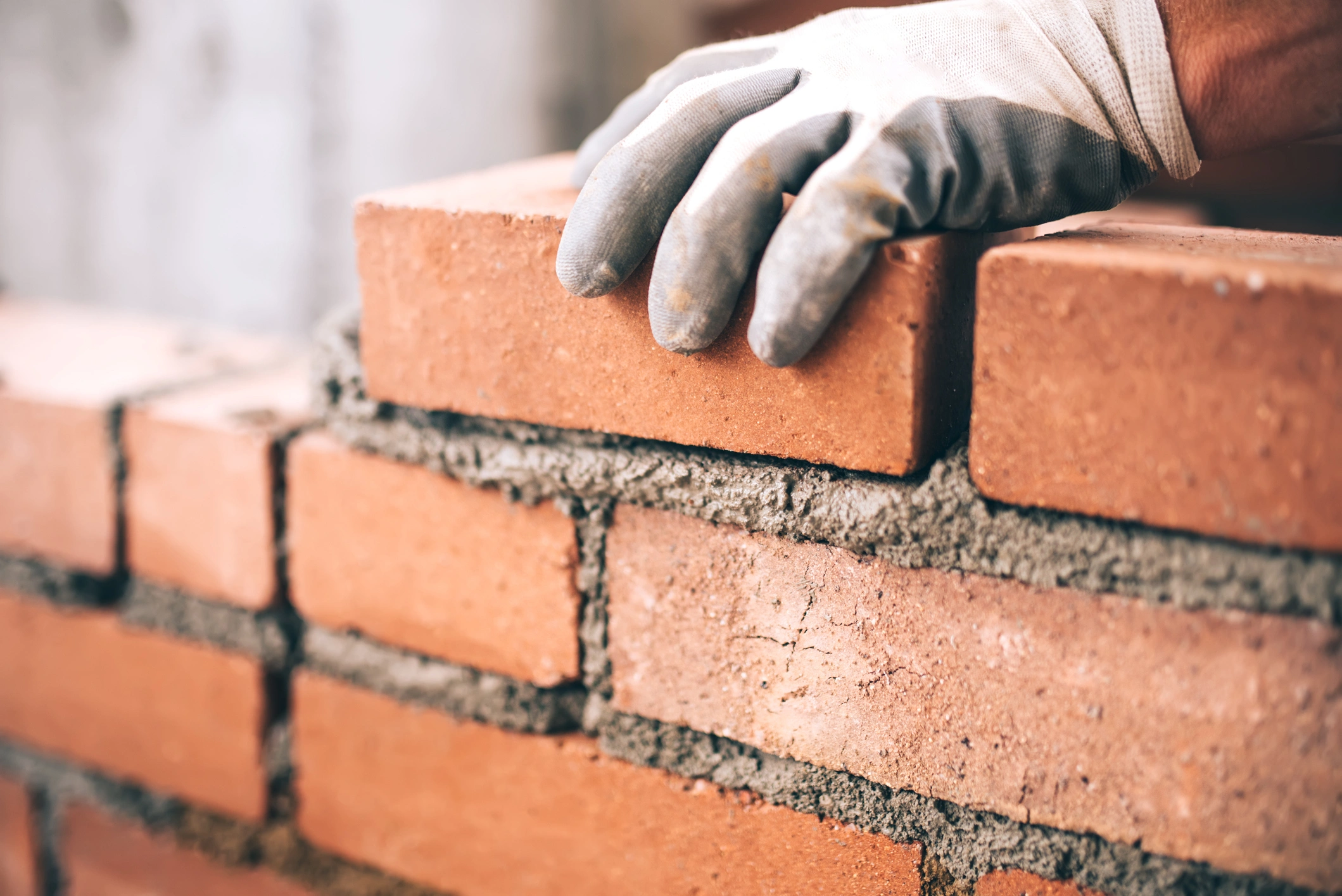 Gloved hand laying a red clay brick with mortar during masonry work