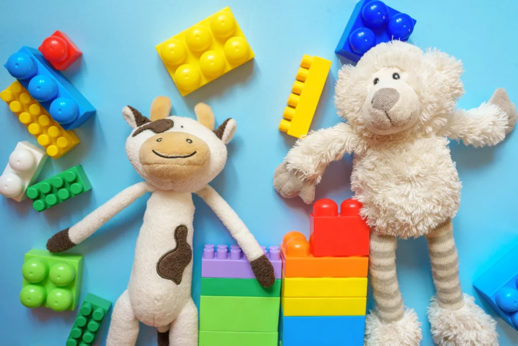 Two stuffed toys (cow and bear) surrounded by colorful plastic building blocks on a light blue surface